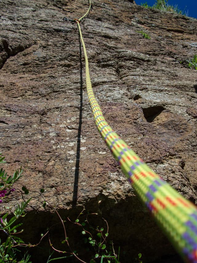 rock climbing rope cliff wall outdoor nature safety sport adventure yellow green blue sky texture rugged vertical ascent equipment challenge recreation landscape ruggedness height perspective terrain vegetation shadow sunlight ruggedness exploration climbing gear
