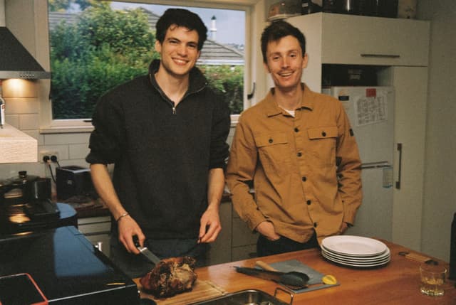 kitchen people smiling cooking food plates countertop knife stove window greenery brown black white glass refrigerator jacket shirt hair cutting board primary color brown