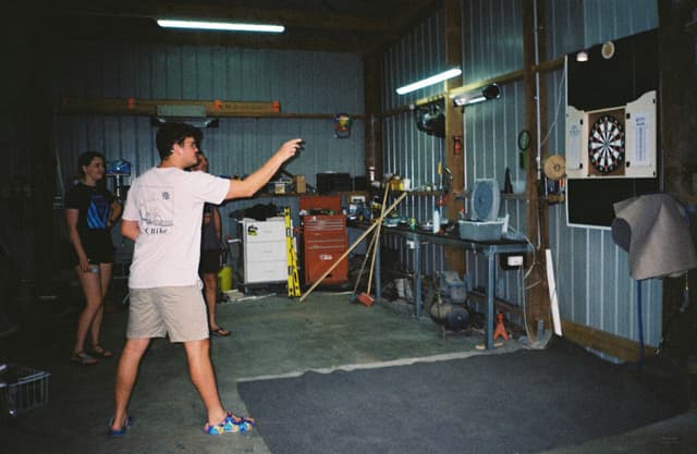 dartboard darts people throwing garage tools equipment shelves broom chair light blue red gray black white floor wall ceiling