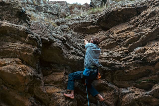 rock climbing climber rocks cliff outdoors adventure sport harness rope nature rugged ascent challenge blue brown vertical movement effort concentration primary color brown