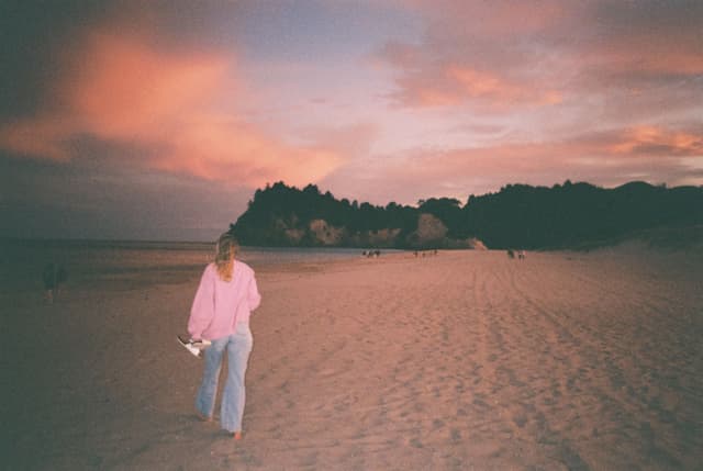 Beach Sand Sky Sunset Clouds Person Walking Pink Shirt Jeans Trees Horizon Landscape Nature Outdoors Dusk Twilight Evening Scenic Silhouette Calm Peaceful Tranquil Serene Relaxing Beauty Coastal Shoreline Primary Color: Pink