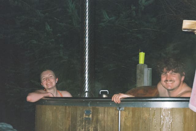 people hot tub wood chimney forest night smile water relaxation outdoor dark brown green yellow towel steam