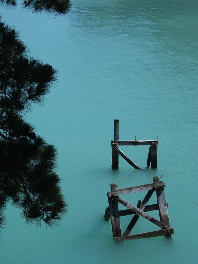 Water Turquoise Tree Branches Wooden Structure Pier Calm Nature Outdoors Reflection Tranquil Scenic Blue Green Sky Peaceful Serene Landscape Abandoned Weathered Old Ruins Stillness Quiet Natural Beauty Environment Tranquility