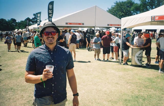 festival crowd tents grass man hat sunglasses drink shirt shorts wristband trees sky blue