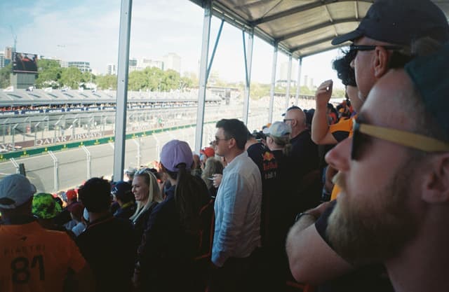 people crowd audience spectators stands race track cars hats sunglasses canopy outdoor event blue sky