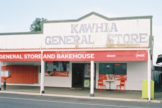 store general bakehouse sign building red white chairs table door window pavement road sky tree