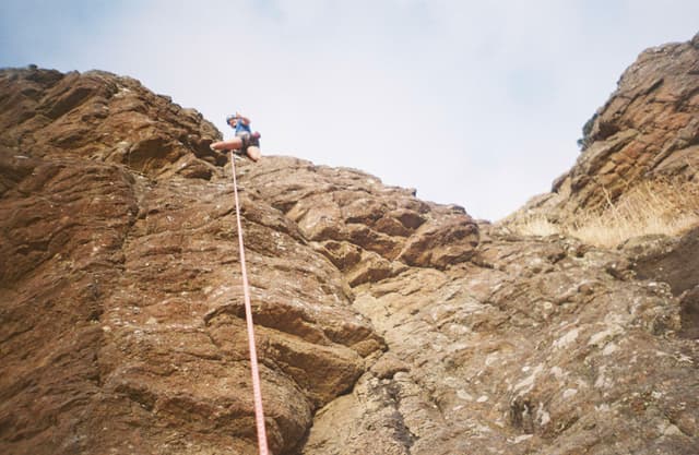 Climbing Rock Climber Rope Mountain Outdoor Adventure Sky Brown Cliff Gear Helmet Harness Blue Rugged Sport Nature Vertical Ascent Challenge Extreme Recreation Landscape Boulder Safety Equipment Steep Terrain Exploration Courage Effort Determination