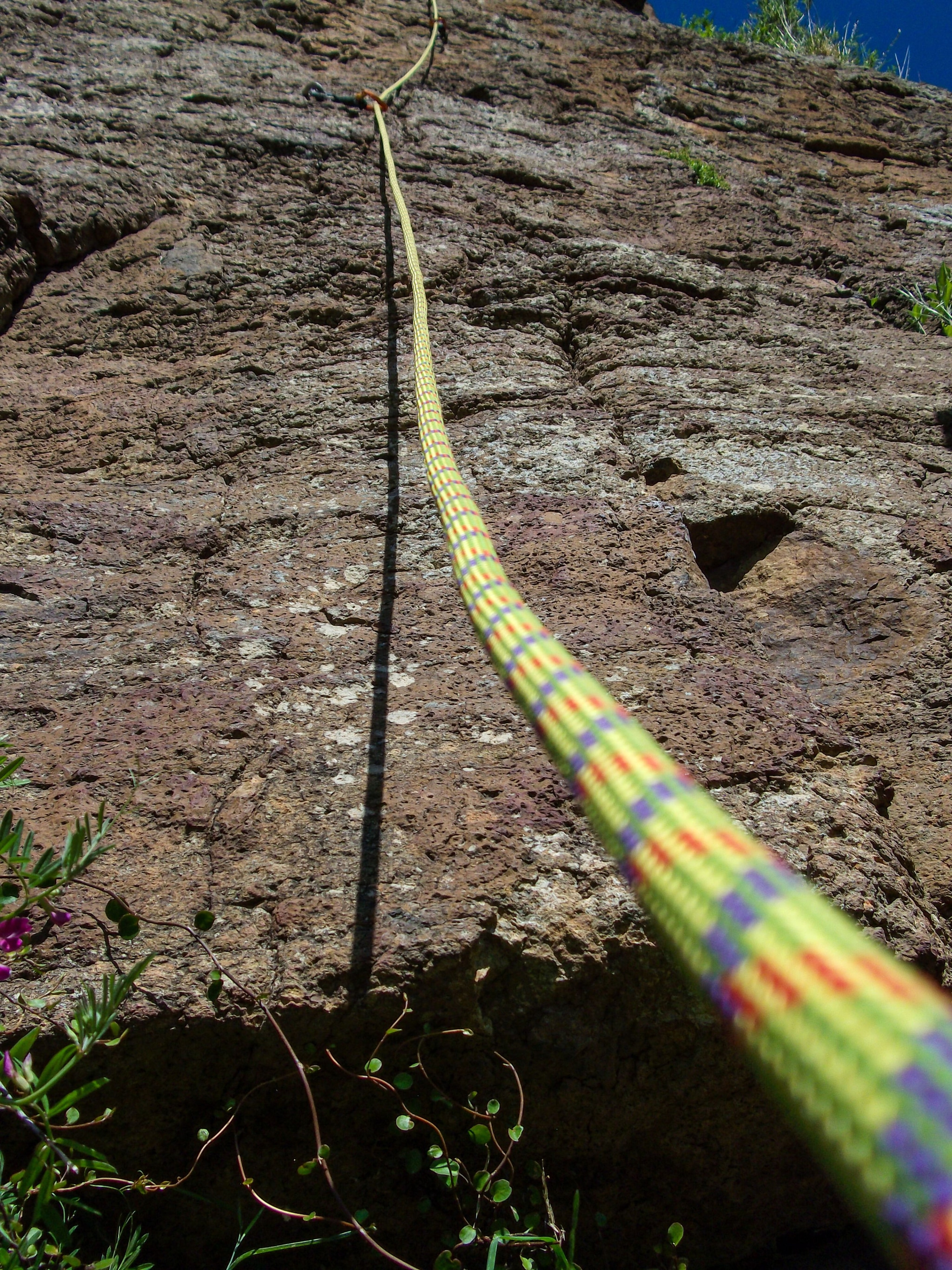 rock climbing rope cliff wall outdoor nature safety sport adventure yellow green blue sky texture rugged vertical ascent equipment challenge recreation landscape ruggedness height perspective terrain vegetation shadow sunlight ruggedness exploration climbing gear