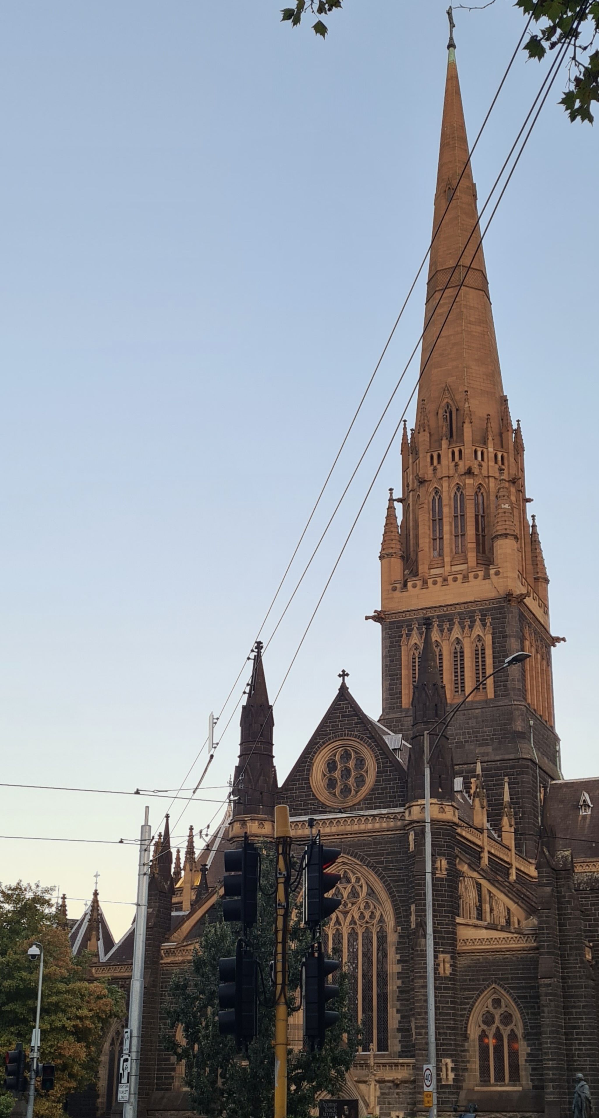 Church Spire Architecture Gothic Building Tower Sky Blue Stone Windows Trees Cross Steeple Historic Landmark Religion Structure Exterior Facade Design Urban Cityscape Sunset Shadows Roof Details Arches Columns Wires