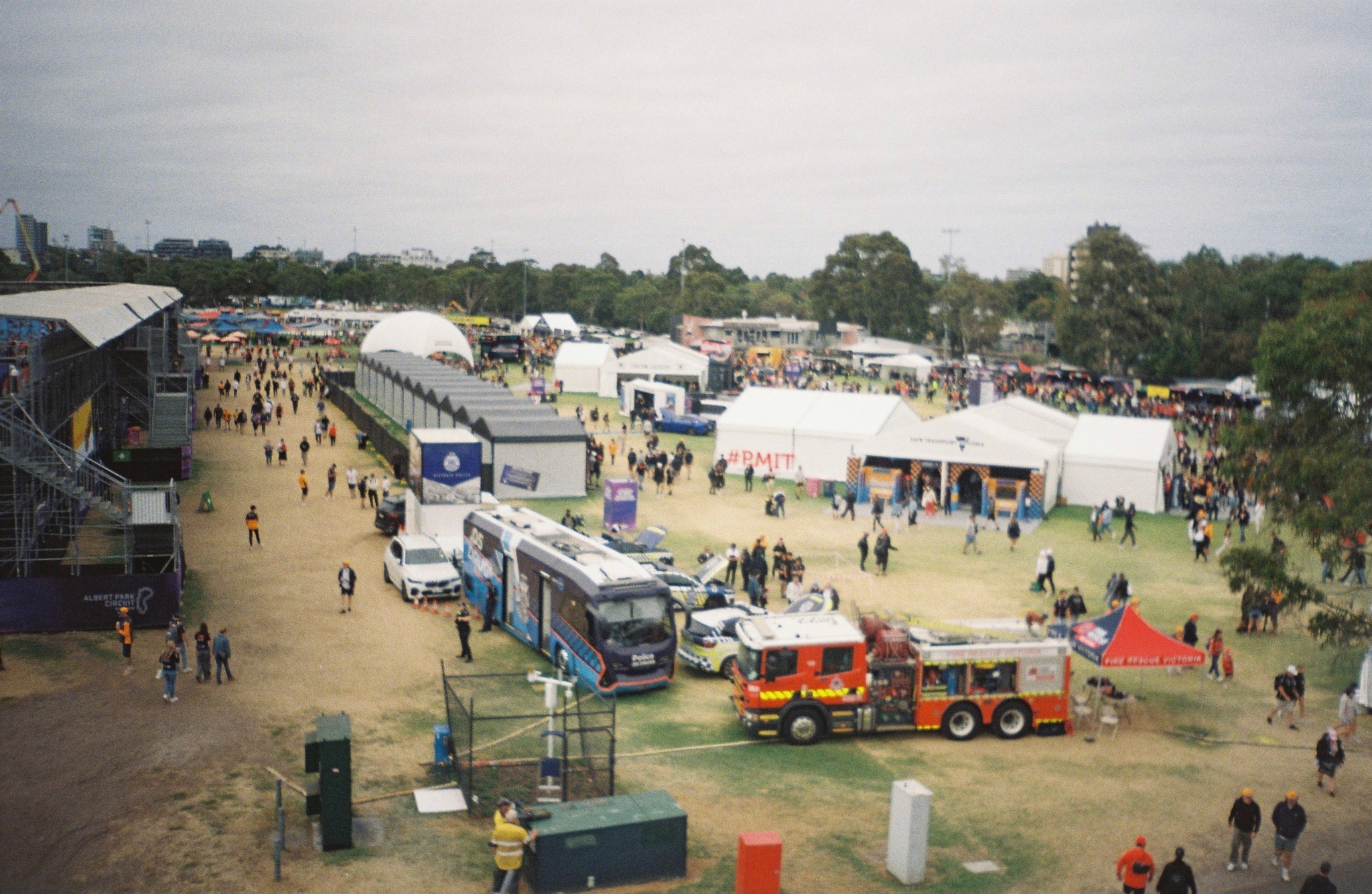 festival event tents people crowd vehicles bus fire truck trees grass sky outdoor daytime primary color green