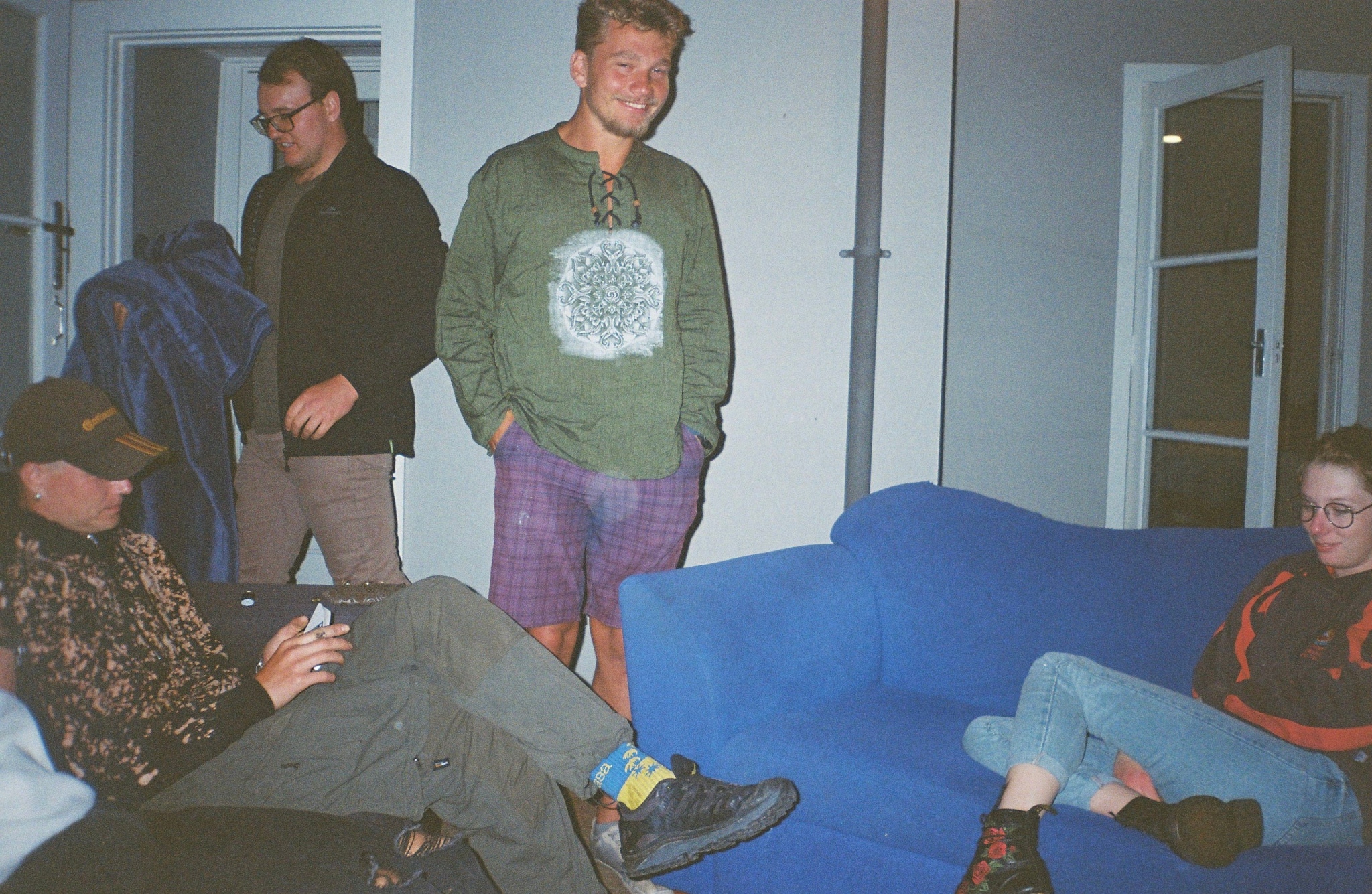 people sitting standing couch blue jacket glasses shoes pants shirt door room indoors casual relaxed conversation gathering furniture