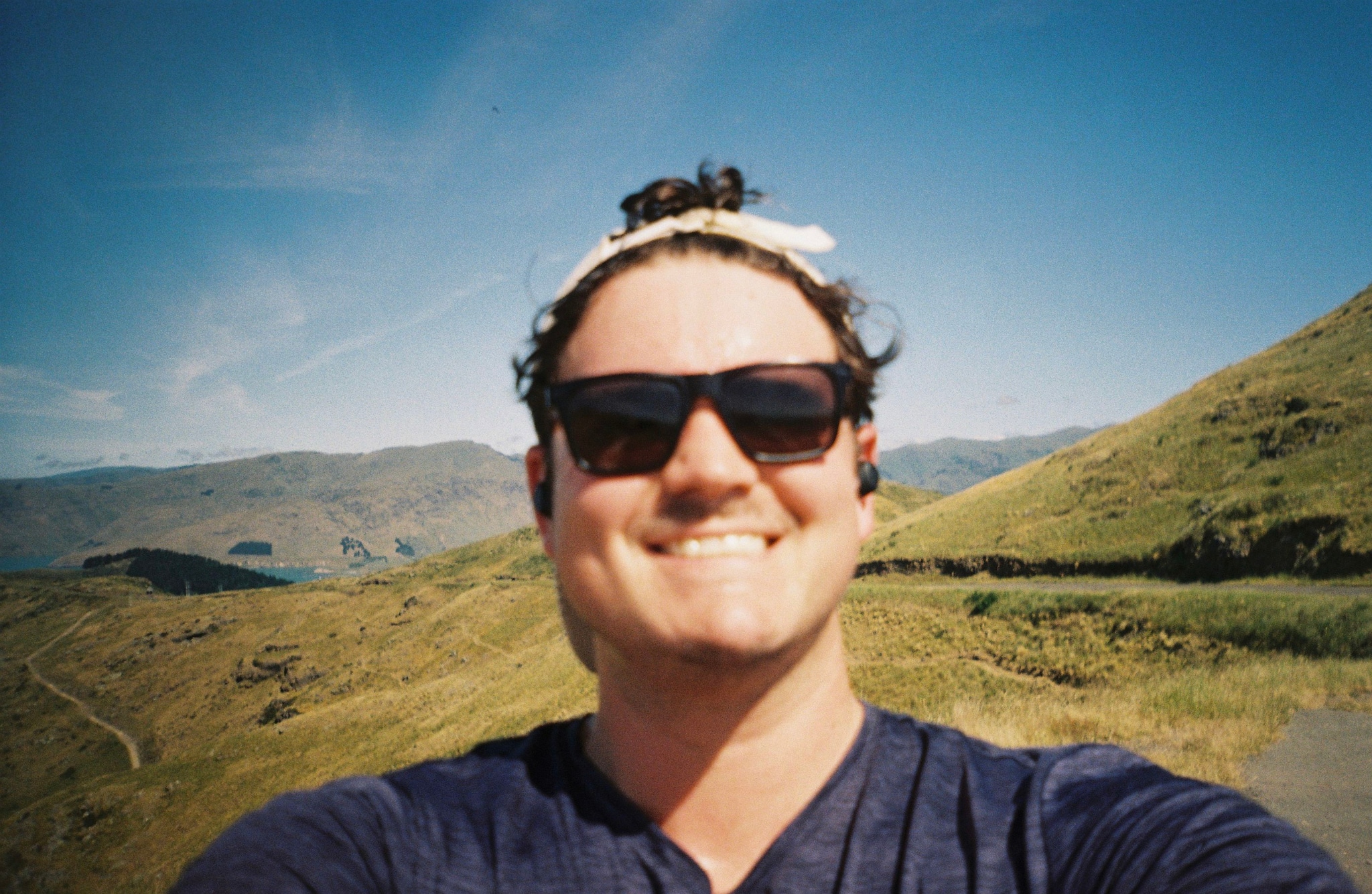 Man Sunglasses Headband Earbuds Smile Mountains Hills Sky Blue Grass Pathway Outdoor Nature Sunny Daylight