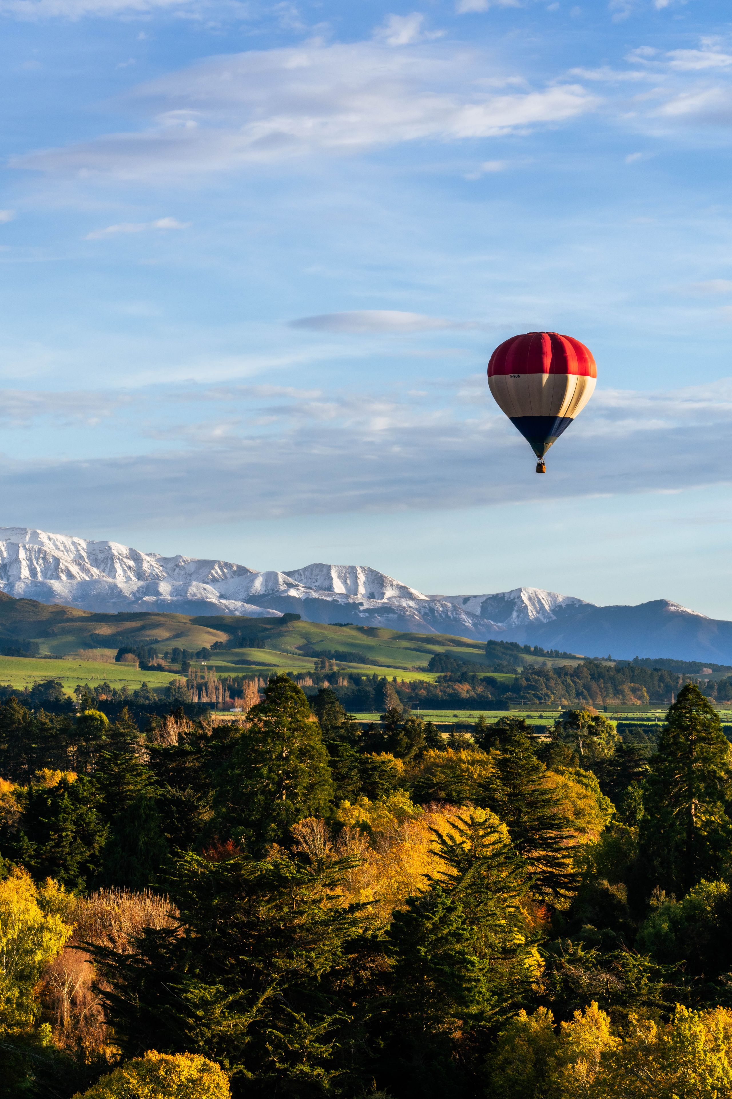 hot air balloon sky landscape trees mountains snow forest greenery blue red white clouds scenery nature travel adventure outdoor aerial view horizon peaceful serene exploration tranquility panoramic vista