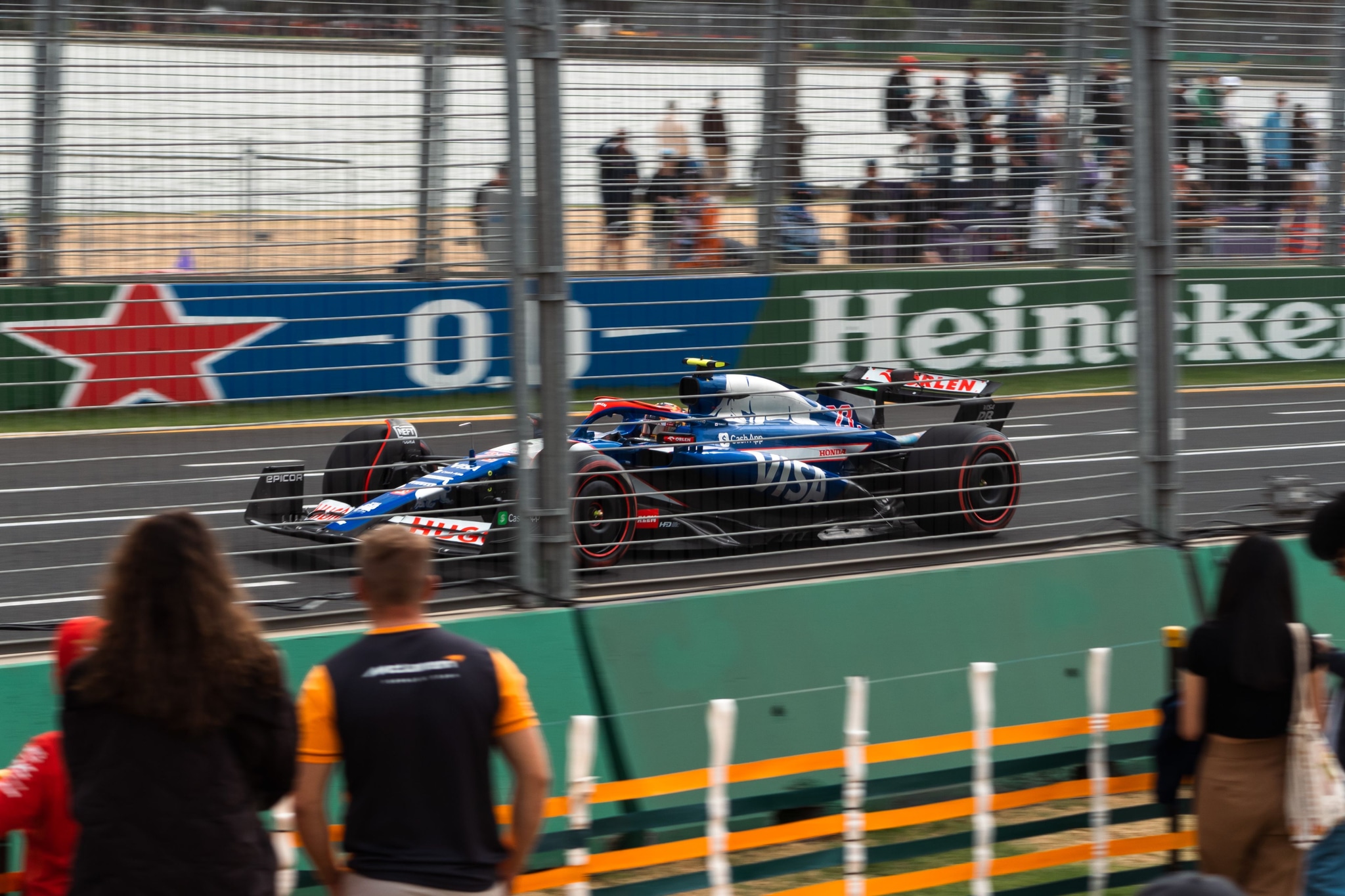 Racecar Track Fence Spectators Advertising Heineken Formula One Motorsport Speed Racing Blue Red White Green Black Asphalt Helmet Driver Crowd Event Competition Barrier Safety Grandstand Signage Fast Action Outdoor Daytime