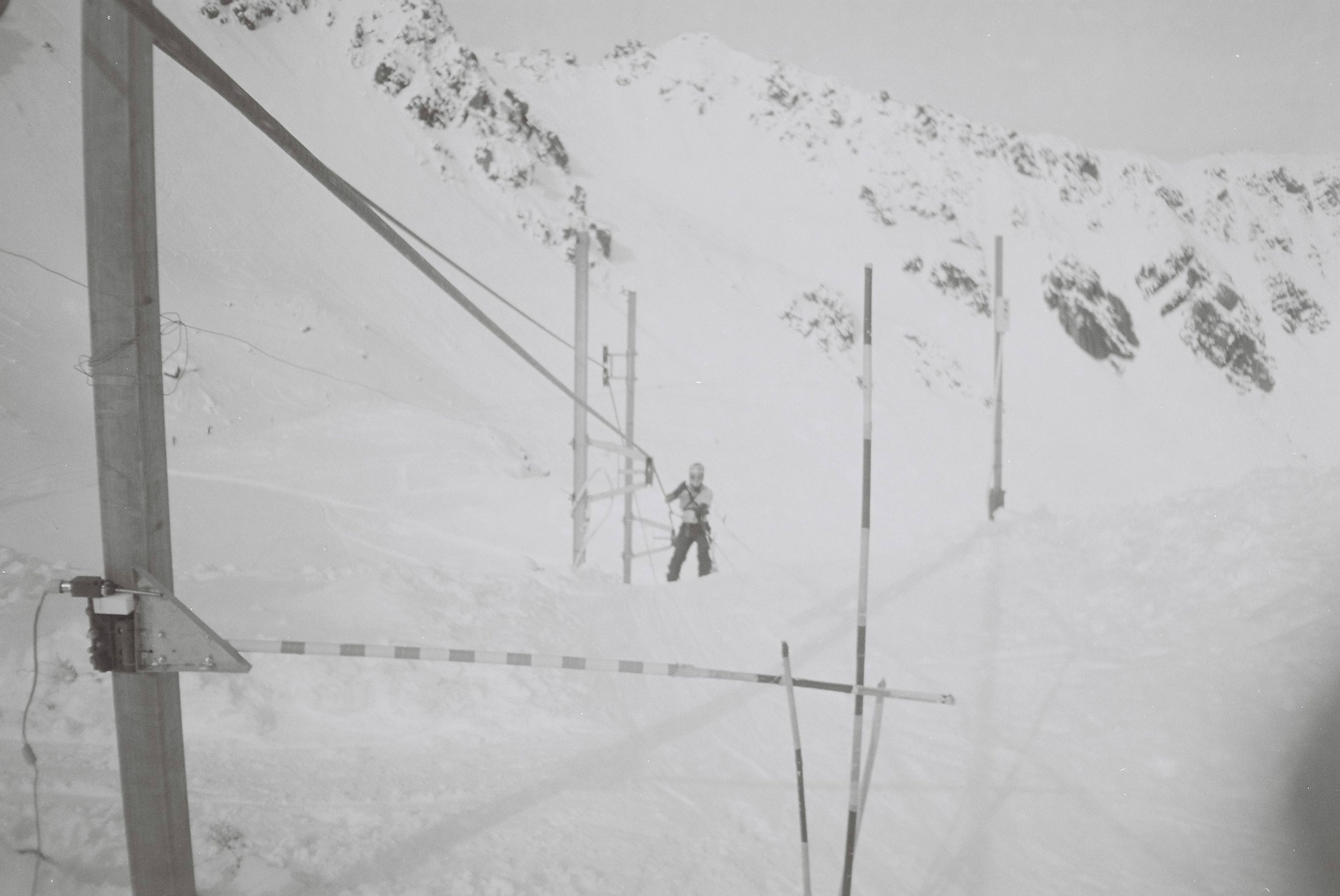 snow mountain ski lift poles cables skier winter white black-and-white landscape outdoor cold slope equipment skiing alpine sport frozen icy remote high-altitude adventure travel recreation nature rugged serene peaceful quiet isolated monochrome vintage retro