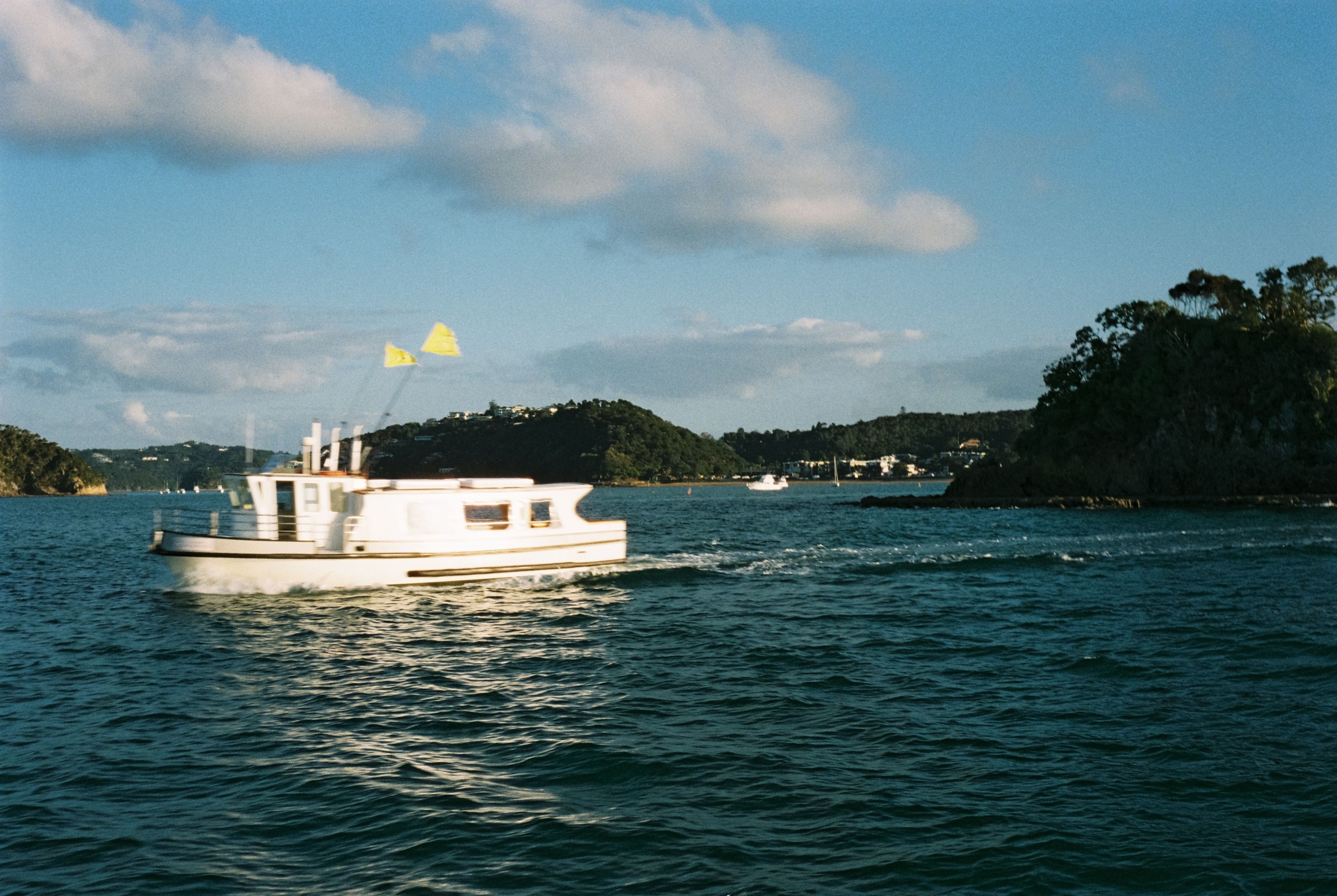boat water sea ocean sky clouds island trees hills landscape white blue green flags sailing nature outdoor travel scenery horizon coast marine vessel