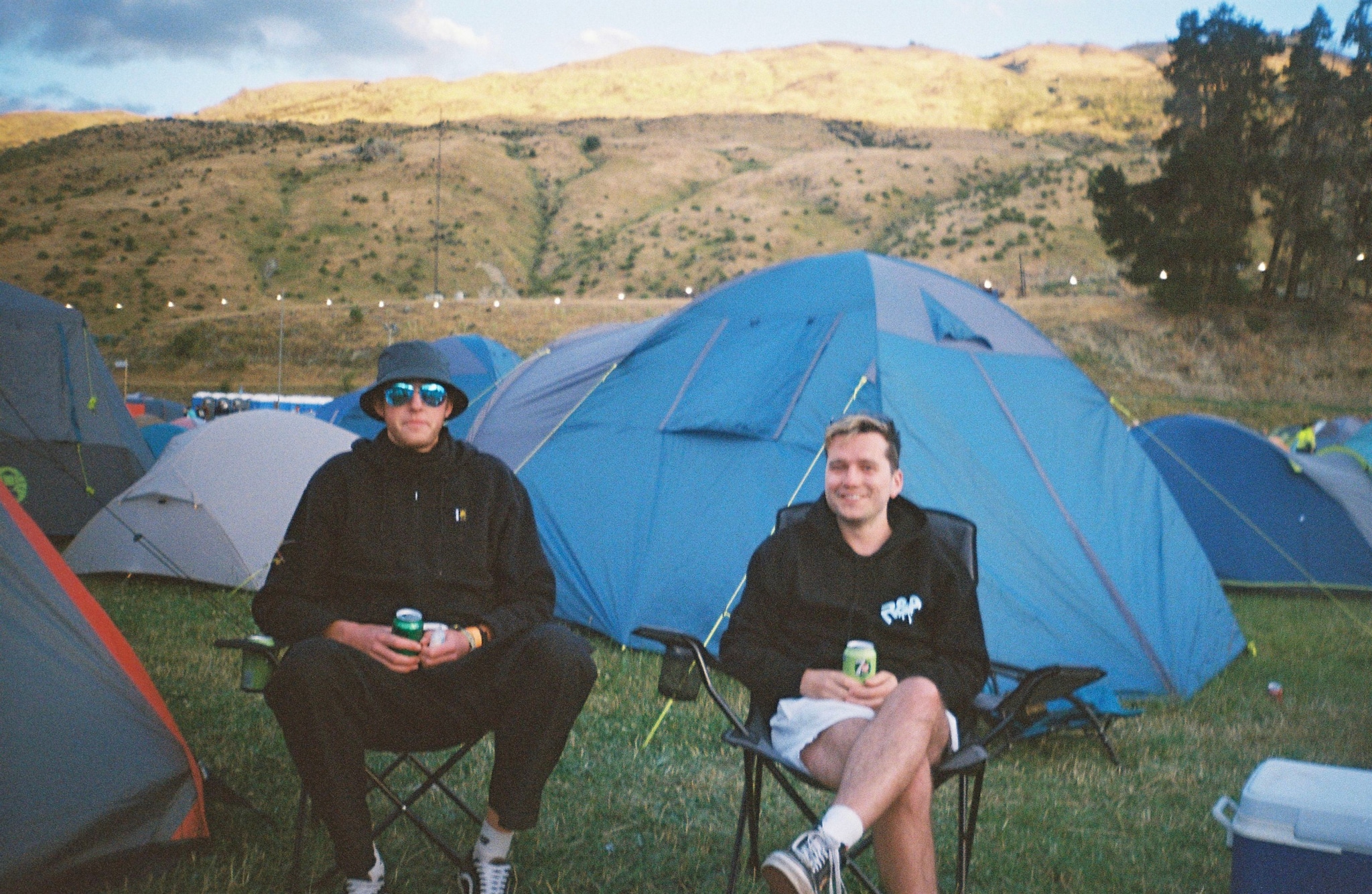 tents camping chairs people grass mountains trees sky blue outdoor nature landscape relaxation leisure festival