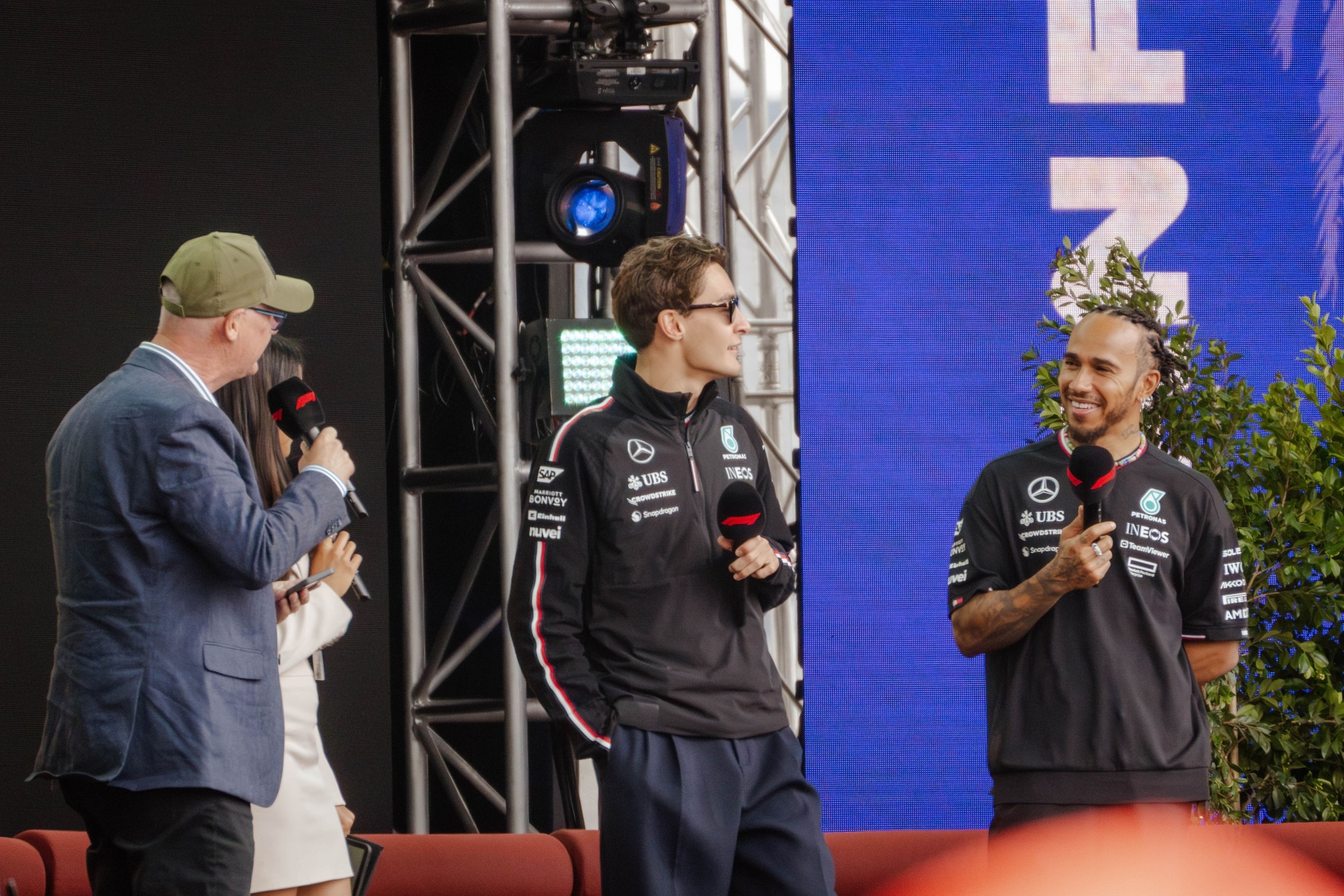 people microphones stage jackets caps blue black red green screen plants chairs event conversation audience