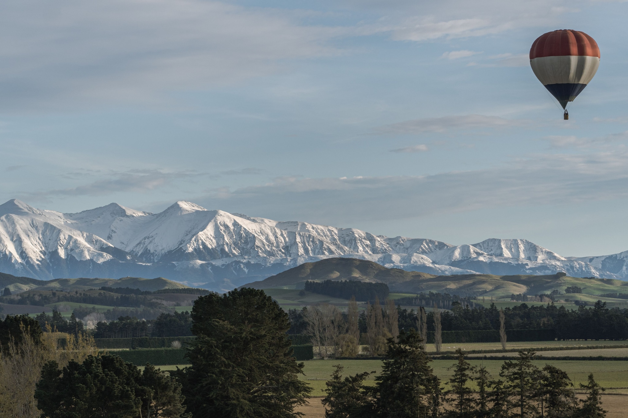 hot air balloon mountains snow trees landscape sky clouds green blue white forest field horizon travel adventure nature outdoor scenic serene peaceful exploration altitude flight aerial view panorama tranquility beauty majestic wilderness rural countryside