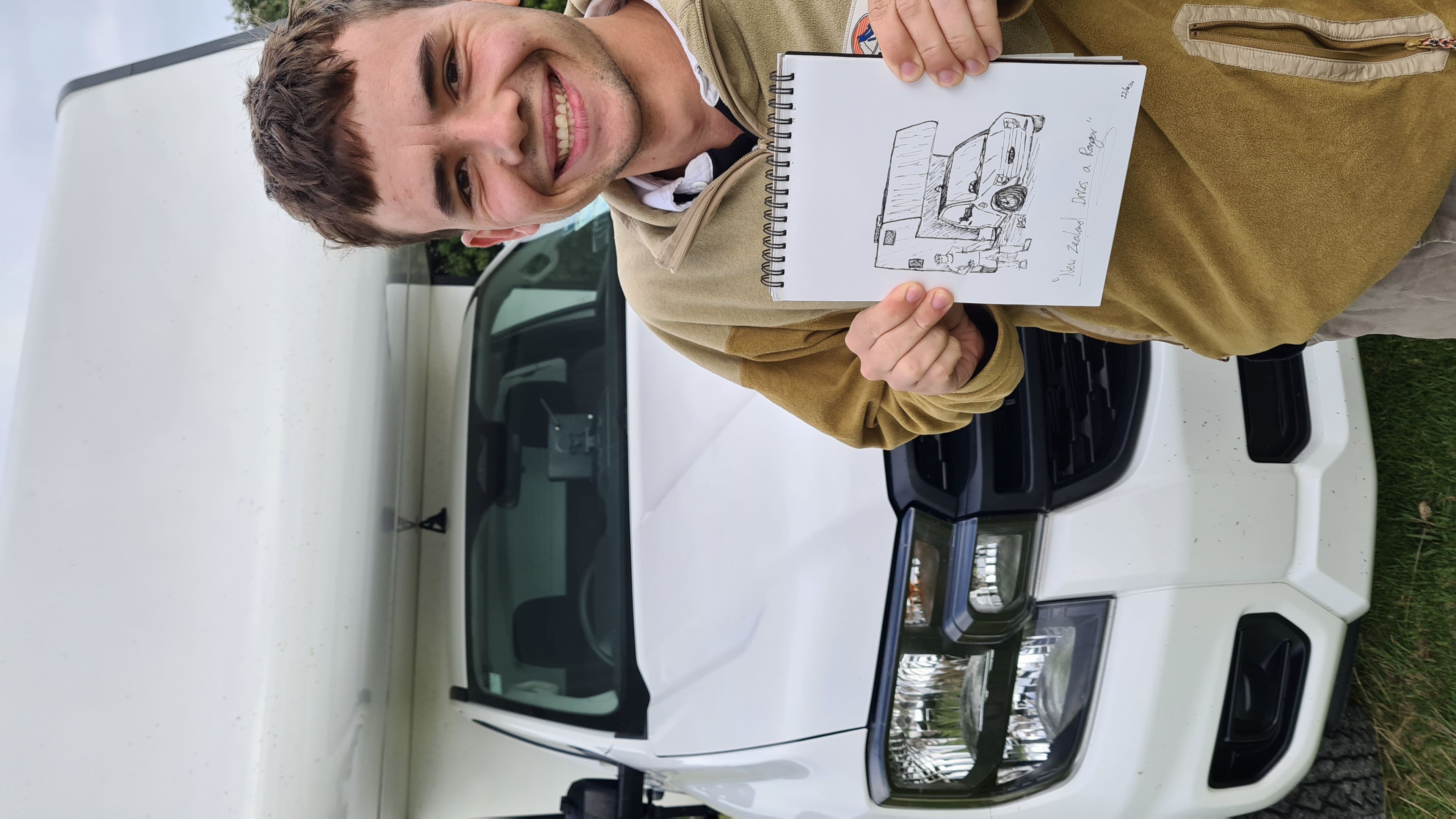 White vehicle van person drawing sketch paper grass outdoors smile headlights front view brown hair beige jacket sky daytime