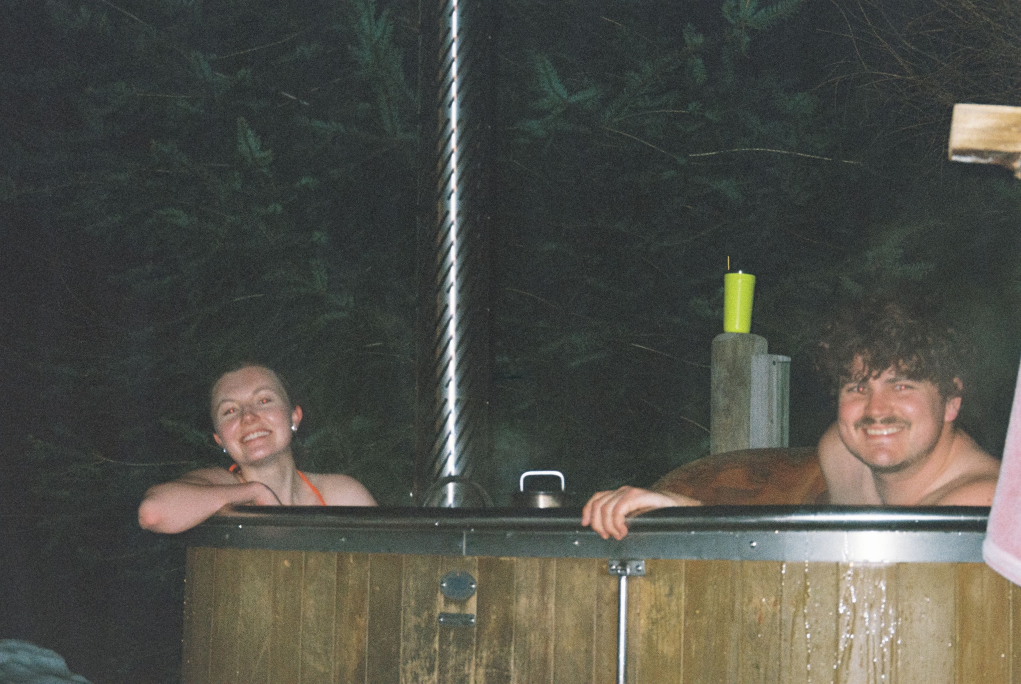 people hot tub wood chimney forest night smile water relaxation outdoor dark brown green yellow towel steam