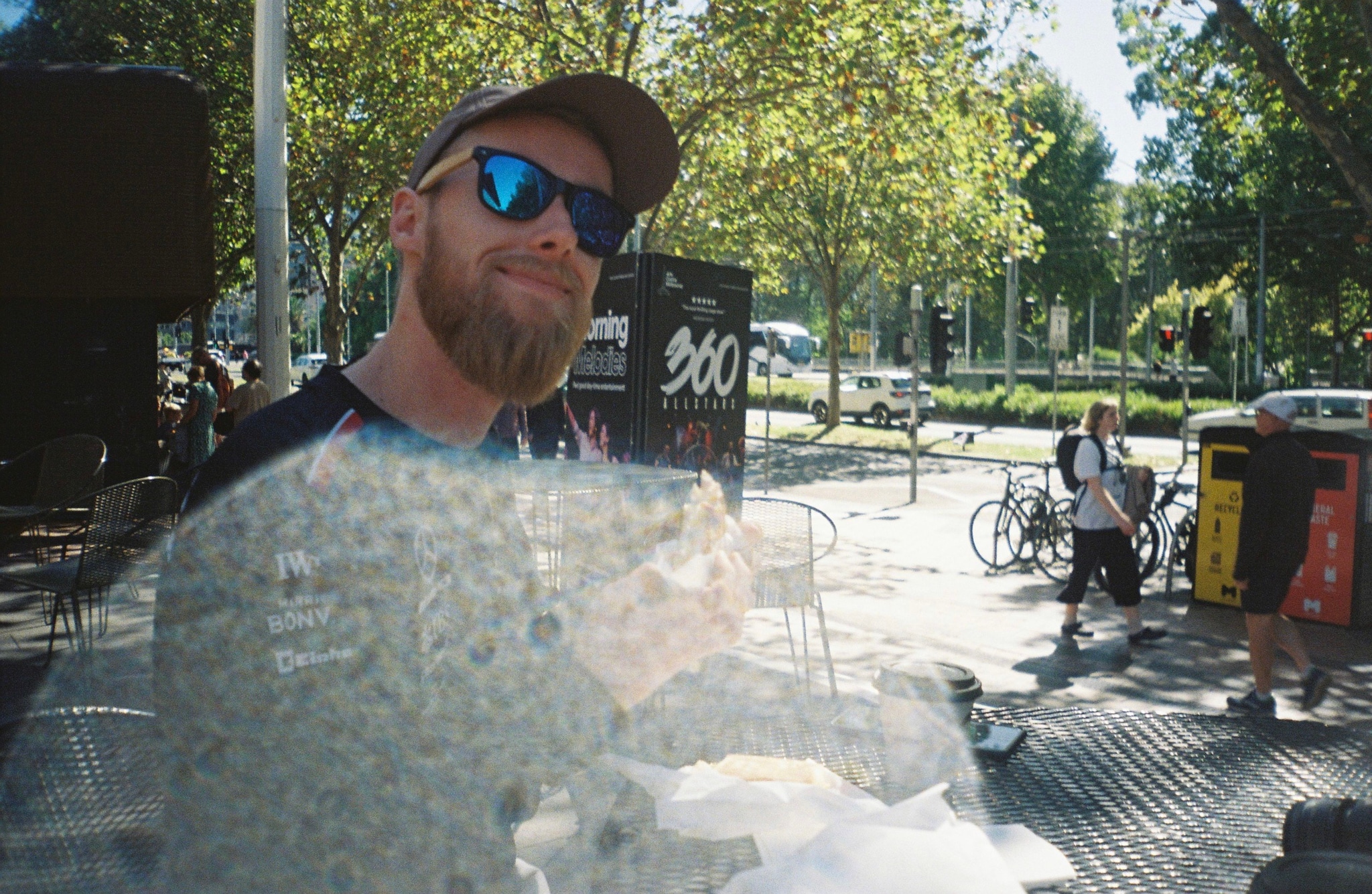 man sunglasses beard cap trees bicycles street sunlight reflection blue green outdoor urban sidewalk people