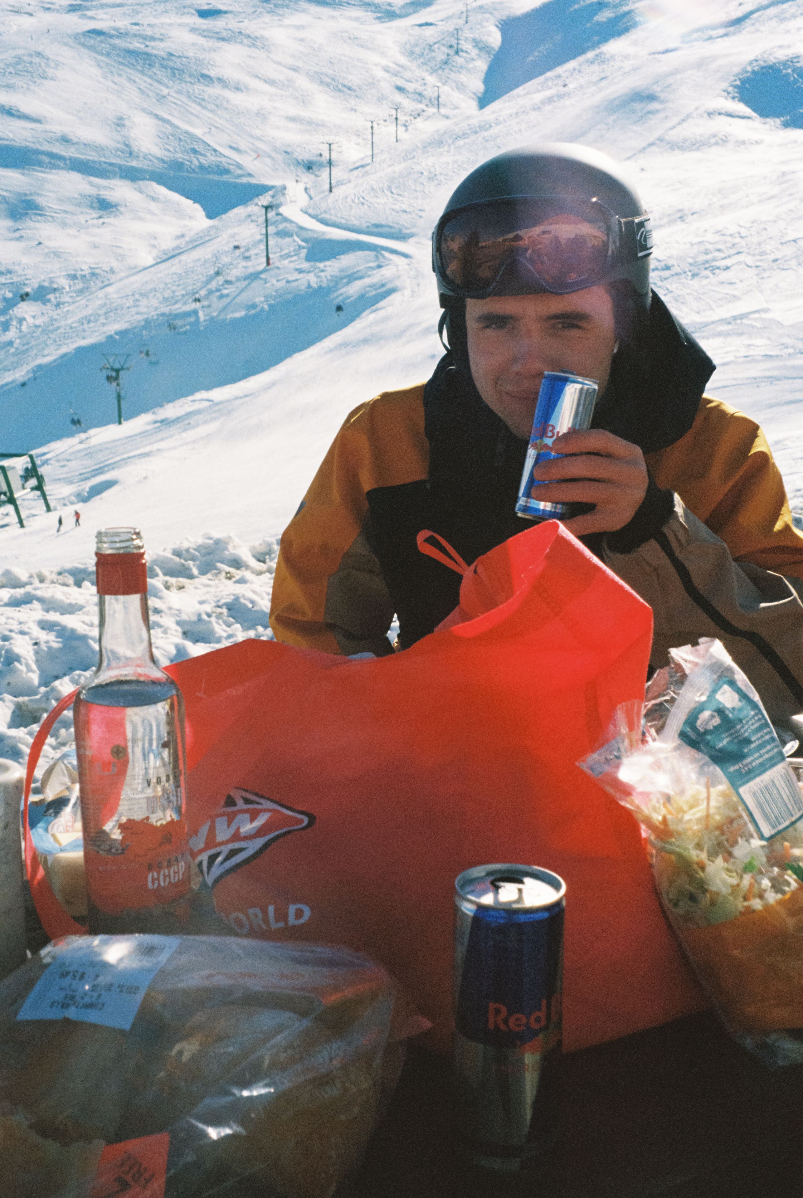 snow helmet goggles jacket person drink can bottle bag bread chips table outdoor winter red white blue sky mountain ski