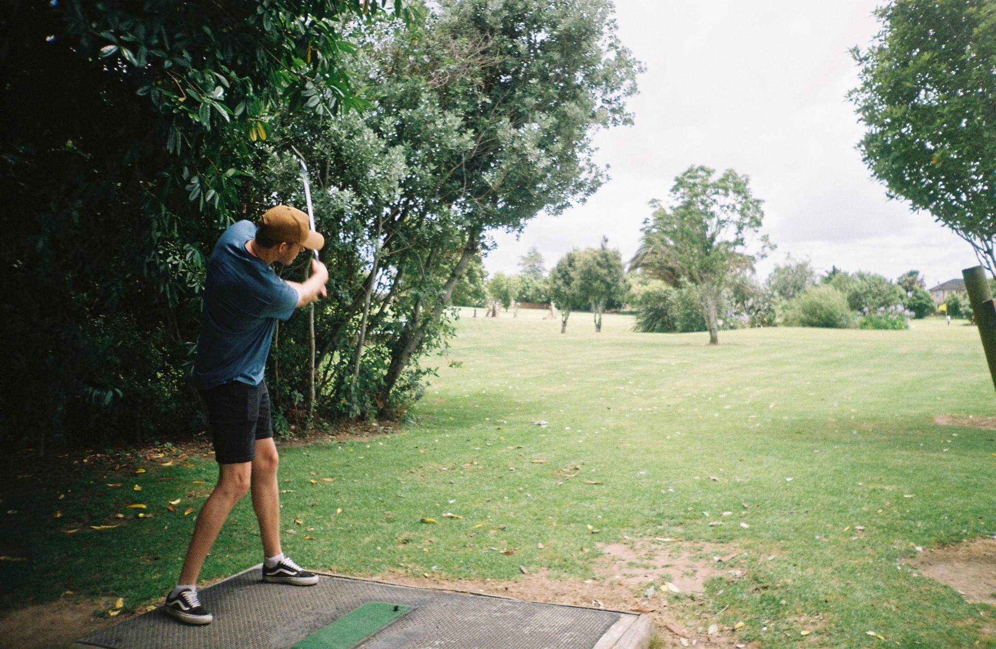 golf golfer swing club course grass trees sky outdoors green blue shorts shoes tee sports action summer nature landscape game recreation leisure activity