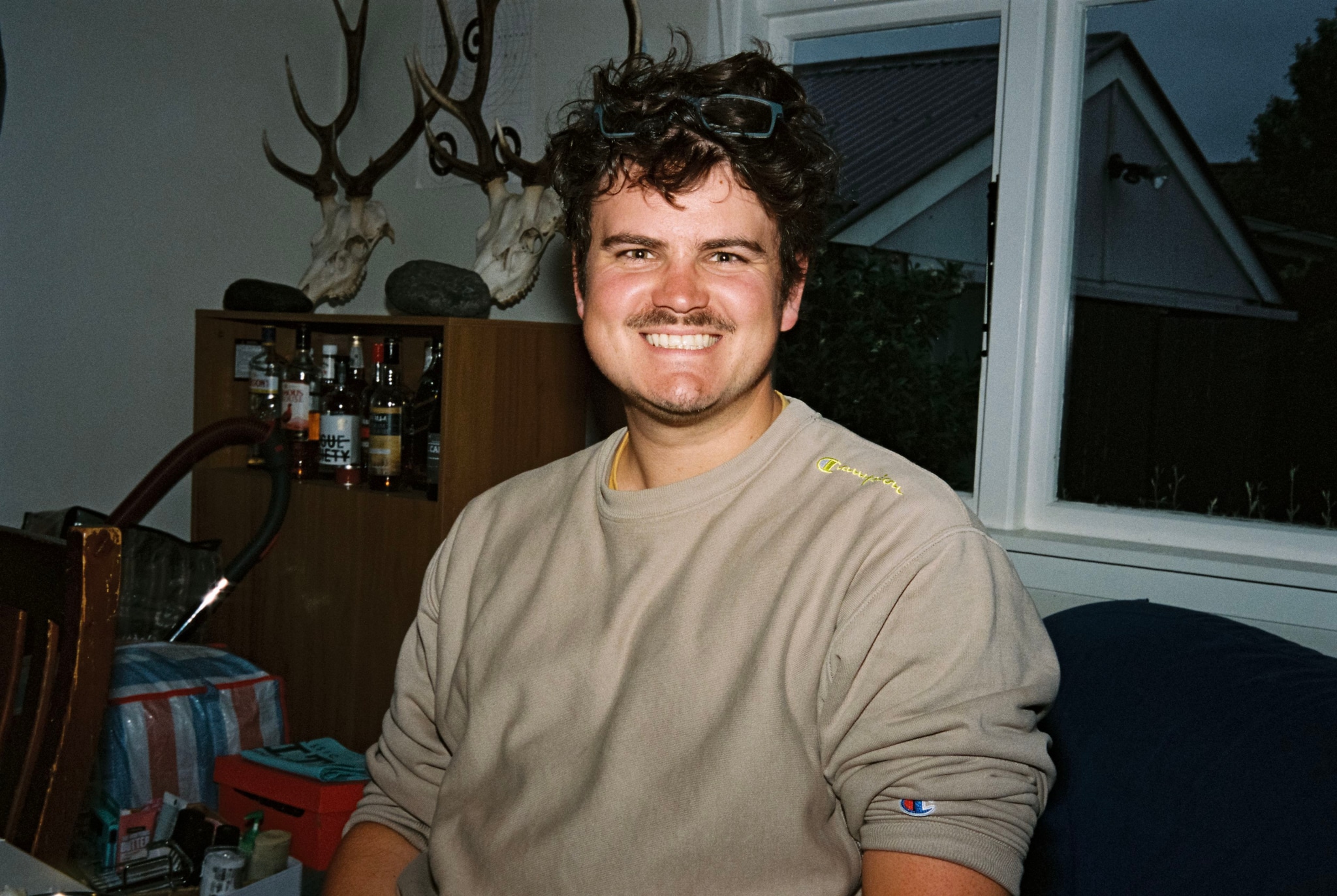 man smile sweater antlers window chair table bottles shelves house interior brown white